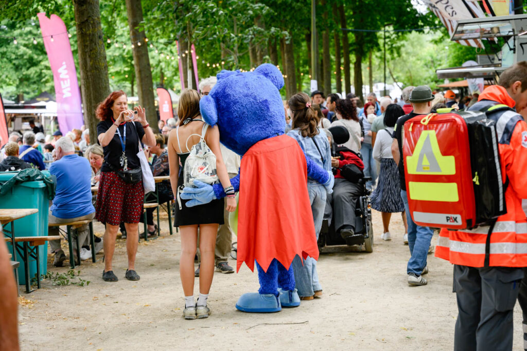 Besucherinnen und Besucher mit Maskottchen auf dem Fest am See 2026.