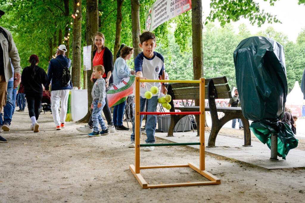 Kind wirft Tennisbälle auf eine Zielwand bei einem Mitmachangebot beim Fest am See 2026.