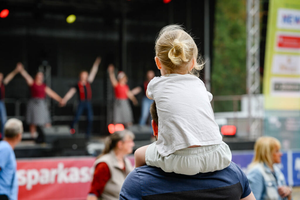 Kind sitzt auf den Schultern eines Erwachsenen und schaut auf die Bühne beim Fest am See 2026.