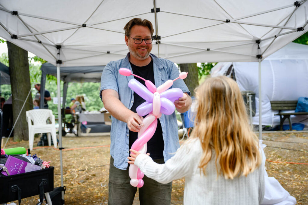 Ballonkünstler überreicht einem Kind eine bunte Ballonfigur beim Fest am See 2026.