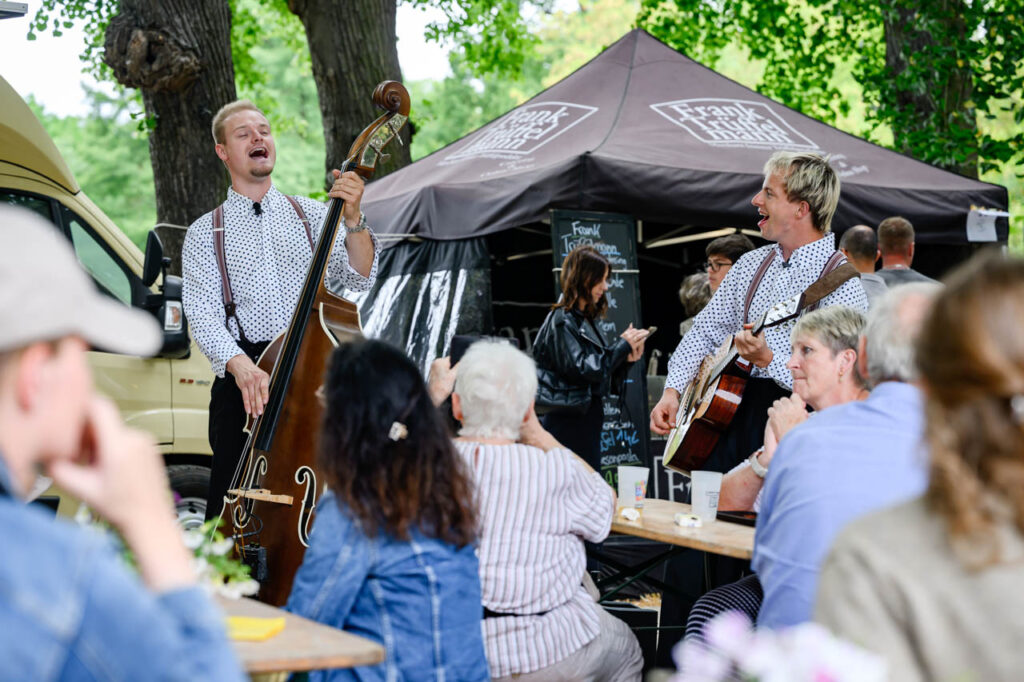 Zwei Musiker spielen mit Kontrabass und Gitarre zwischen den Gästen beim Fest am See.