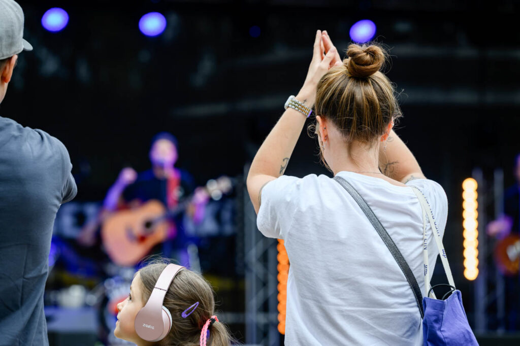 Besucherin applaudiert vor der Bühne, während ein Kind mit Gehörschutz die Live-Musik beim Fest am See verfolgt.