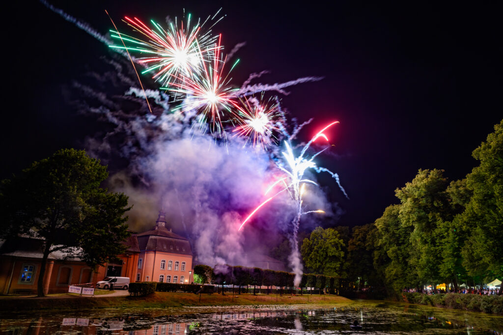 Feuerwerk mit verschiedenen Farben über Wasserfläche und Bäumen in Mönchengladbach.