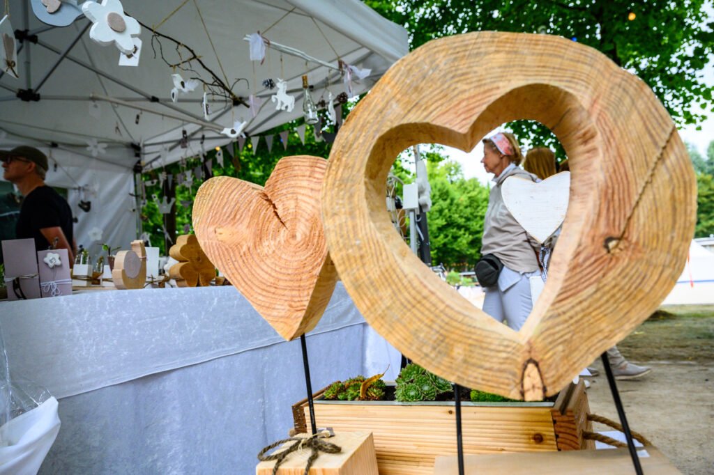 Holzdekorationen in Herzform auf einem Marktstand, handgemachte Produkte im Vordergrund.