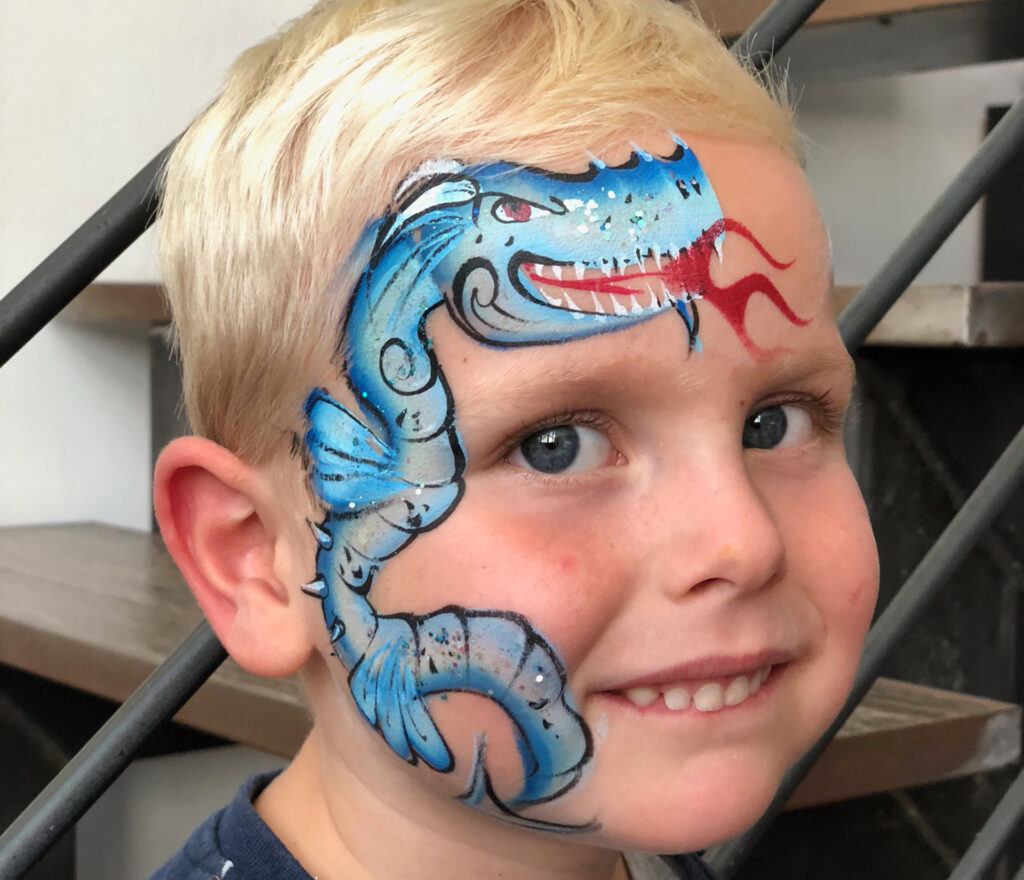 Ein Kind mit blauer Drachen-Gesichtsbemalung mit roten Flammen schaut in die Kamera
